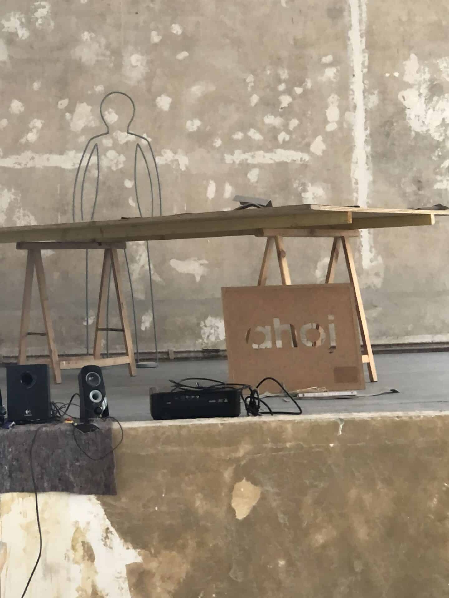 Minimalistische Kunstinstallation mit Tisch und Metallskulptur vor Wand.