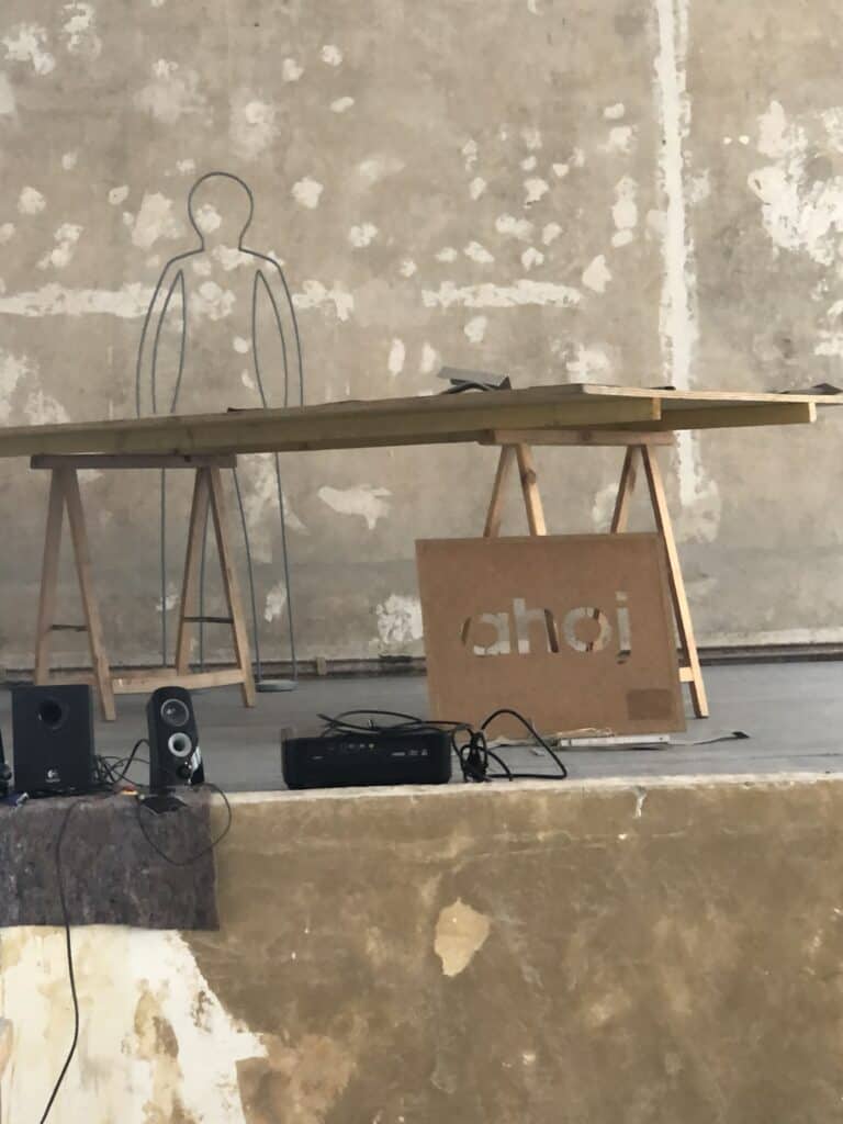 Minimalistische Kunstinstallation mit Tisch und Metallskulptur vor Wand.