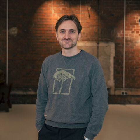 Mann in gemütlichem Raum mit Backsteinwand im Hintergrund.