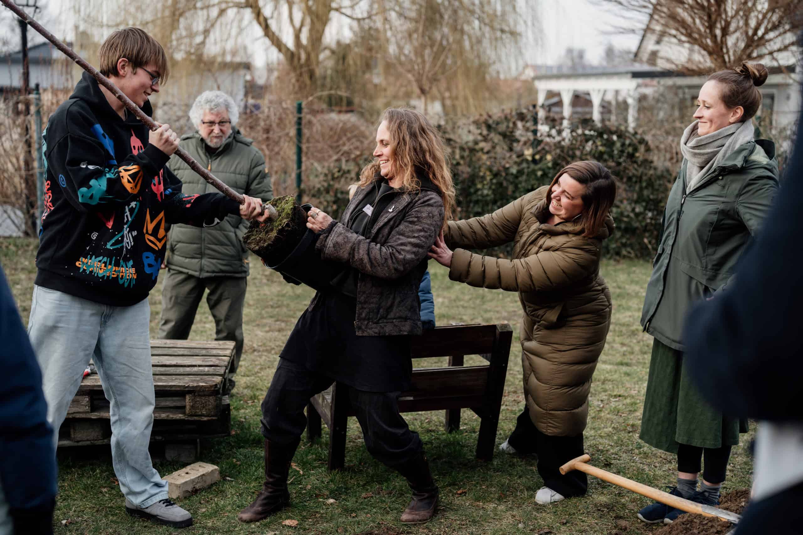 Menschen beim spielerischen Kampf mit Stöcken im Garten, bei AngerWERK.