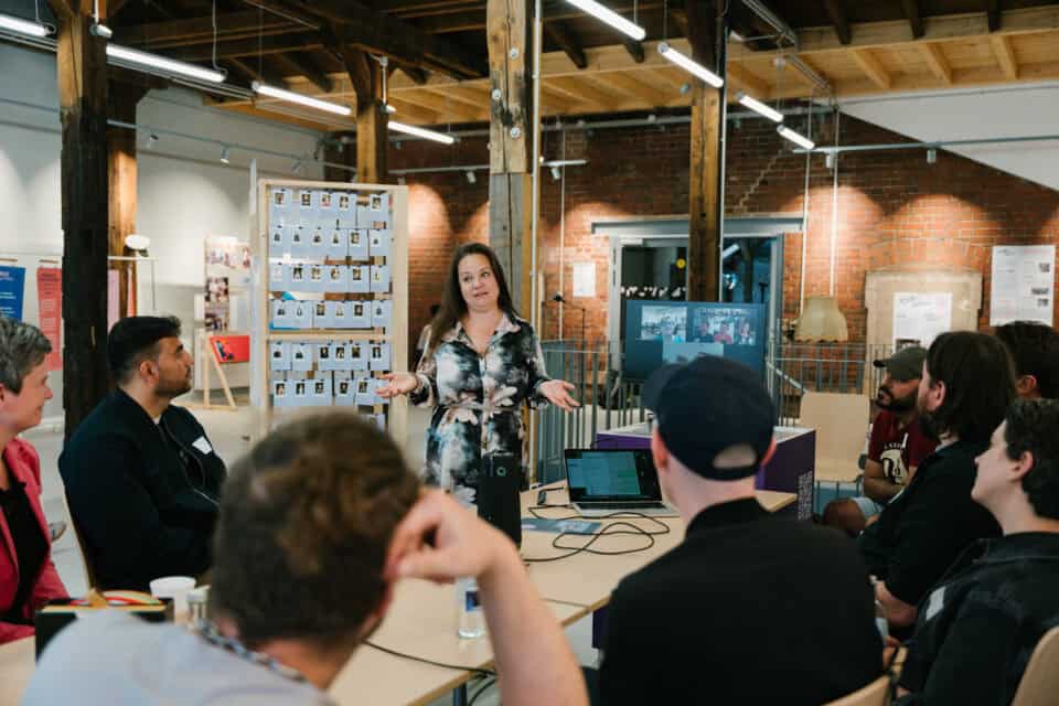 Frau präsentiert Projekt vor Team in kreativem Arbeitsraum, interaktive Diskussion.