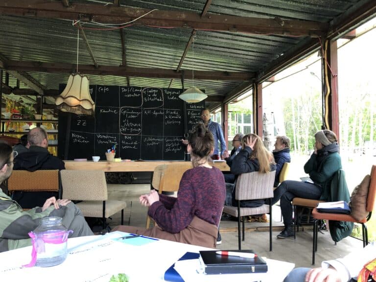 Gruppenunterricht in einem offenen, lichtdurchfluteten Raum mit Tafel und Teilnehmern.