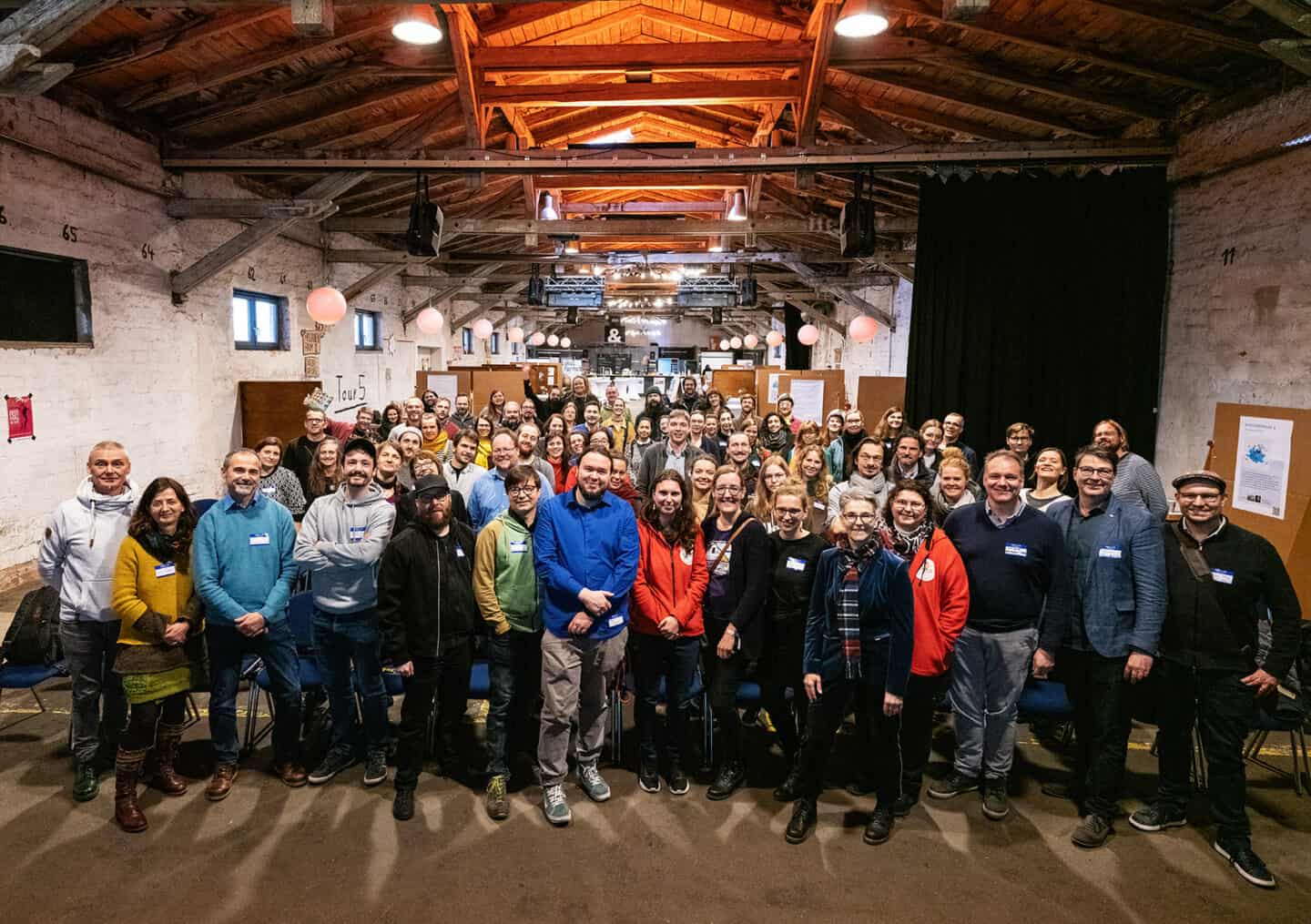 Große Gruppe von Menschen bei einem Treffen in einem rustikalen Veranstaltungsraum.
