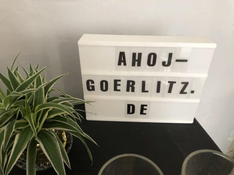 Lichtbox mit "Ahoj Görlitz" auf einem Tisch neben einer Pflanze.