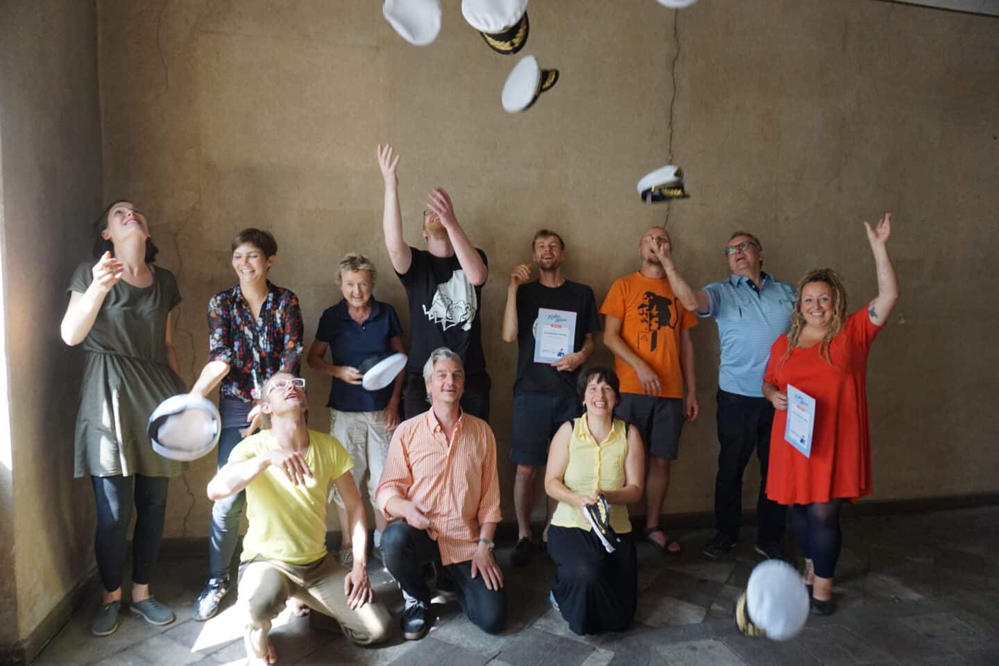 Gruppe von Menschen beim Hutwerfen in einem Raum, lachend und fröhlich.