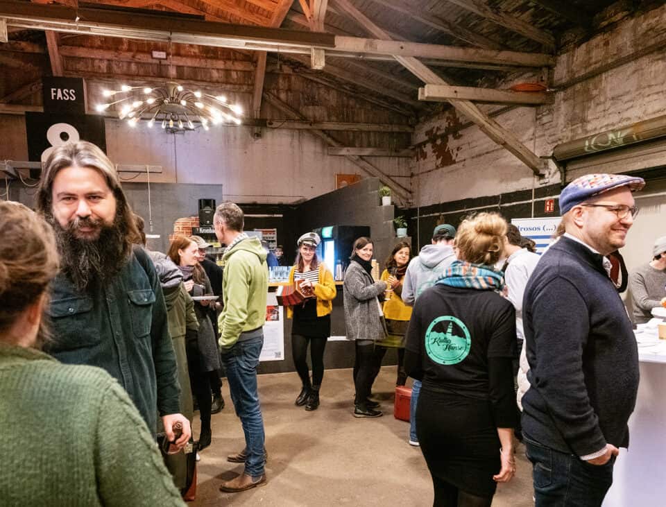 Menschen bei einer Kunstmesse in einem Industriegebäude, Gespräche und Ausstellungen.