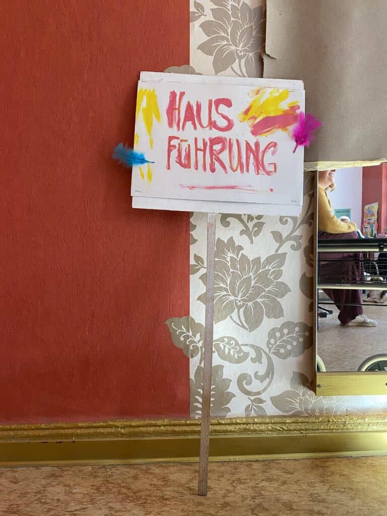 Hausführung Schild in Angermünde, handgemalt mit bunten Federn.